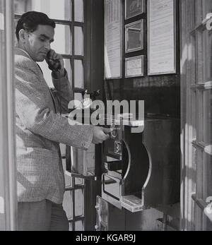 Début des années 1950, photo historique montrant un homme d'outre-mer pour l'Angleterre d'effectuer un appel à partir d'un téléphone public fort dans Kensington Gore, Londres. Ayant mis ses pièces de monnaie dans, il est sur le point d'appuyer sur le bouton A lorsque le récepteur répond à son appel. Banque D'Images