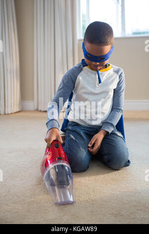 Garçon en costume de super-héro le nettoyage d'un étage à l'aspirateur à la maison Banque D'Images