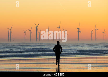 Jogging sur la plage de Seaton Carew au lever du soleil avec le parc éolien Teesside Offshore en arrière-plan, côte nord-est de l'Angleterre. ROYAUME-UNI Banque D'Images