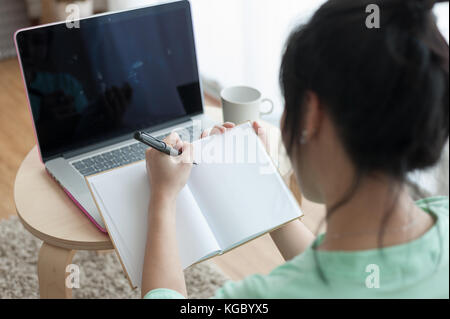 Jeune asiatique attrayant femme gauchère freelancer écrit sur un ordinateur portable tout en travaillant avec un ordinateur portable. travailler à la maison et de l'apprentissage en ligne concept Banque D'Images