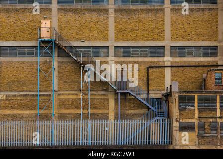 Bâtiment industriel délabré avec façade de brique jaune blue rusty fire escape staircase atteignant plus de 3 étages. Banque D'Images