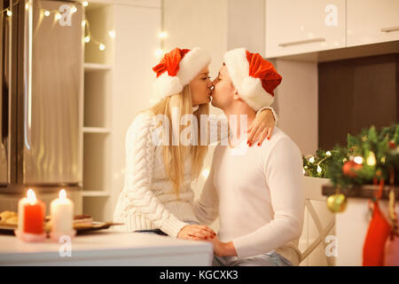 Un couple à santa claus hats baisers le jour de Noël. Banque D'Images