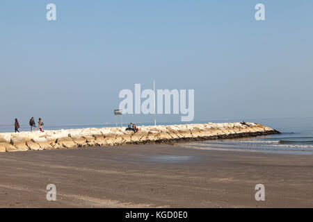 Personnes pour le coucher du soleil à Blue Moon Beach, Lido, Venise, Italie détente sur la jetée en pierre ou sur un mur de défense côtière soirée ensoleillée d'automne Banque D'Images