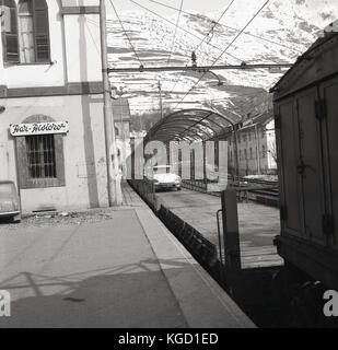 Années 1950, tableau historique des voitures sur les wagons à ciel ouvert d'une voiture (train couchettes) arrivant dans la région de Meran Trentino-Alto Adige, Italie. C'est une méthode populaire de transport des personnes et des véhicules à travers l'Europe en ce moment. Banque D'Images