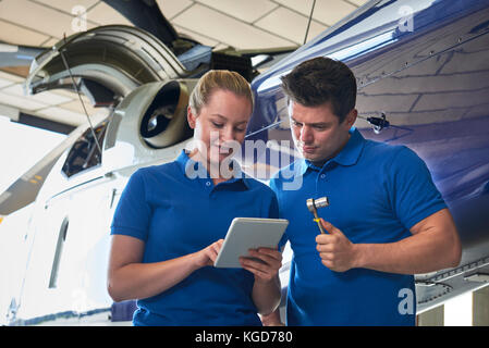 Ingénieur aero et apprenti travaillant sur hélicoptère dans hangar looking at digital tablet Banque D'Images