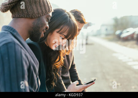 Trois hommes et femmes multiethniques en plein air d'amis ville lumière arrière, bavarder et holding smart phone - amitié, réseau social, concept Banque D'Images