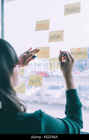 Young business woman standing in front of glass wall avec post it - entreprise, d'équipe, concept de réflexion Banque D'Images