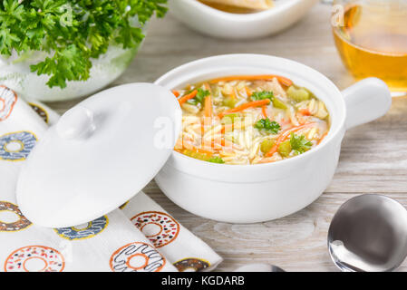 Soupe de poulet l'orzo dans une cruche blanche sur fond de bois. L'italien orzo de soupe. Banque D'Images