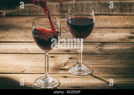 Verser le vin rouge dans un verre sur une table en bois Banque D'Images