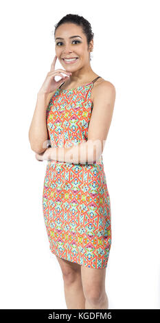 Femme brésilienne est souriante. Un bras s'enroule autour de la taille et la main repose sur le menton. femme avec de courts cheveux bouclés portant robe colorée de l'été. Banque D'Images