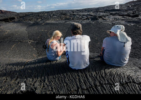 Une famille de touristes s'assied pour se reposer et discuter sur une coulée de lave dans les îles Galapagos. Banque D'Images