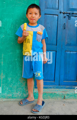 Smiling boy eating népalais doux traditionnel en face d'une maison colorée, Bandipur, Tanahun district, Népal Banque D'Images