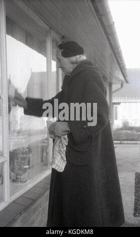 Années 1950, historique, dame âgée dans overcoast nettoyage extérieur d'une fenêtre, England, UK. Banque D'Images