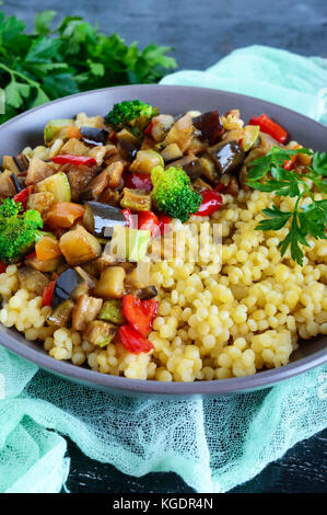 Un régime alimentaire léger plat végétalien : couscous et légumes (courgettes, aubergines, carottes, poivrons, oignons, persil) sur un fond noir. Banque D'Images