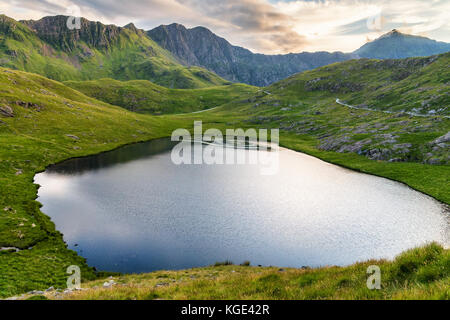 Lac appelé Llyn Teyrn sous randonnées chemin vers Snowdon pic de mineur, appelé la voie, le Pays de Galles, Grande-Bretagne. Coucher du soleil douce et chaude lumière reflétée dans cool blue Banque D'Images