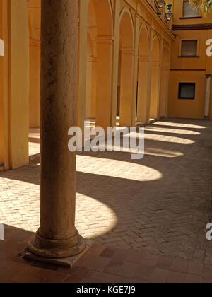 Pilier debout devant les ombres d'arches jeté sur une cour pavée au Royal Alcázar de Séville, Real Alcázar de Sevilla, Espagne Banque D'Images