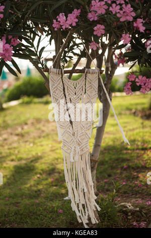 Shot verticale de macrame wall art hanging from tree oleander, tourné avec une faible profondeur de champ Banque D'Images