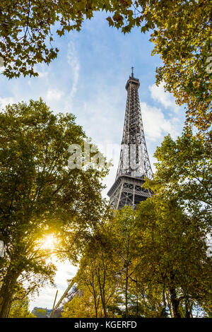 Vue de dessous de la Tour Eiffel entre les arbres en premier plan avec le coucher de soleil éclatant à travers le feuillage. Banque D'Images