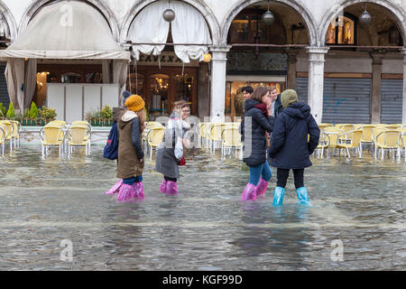 Venise, Vénétie, Italie. Nov 7, 2017. Acqua Alta marée haute de 115cm à partir de la lagune provoquant des inondations temporaires sur la Piazza San Marco. Un groupe d'amis aux éclaboussures dans l'eau de porter des couvre-chaussures jetables en plastique coloré à l'avant de la fermé Caffe Lavena. Credit : Mary Clarke/Alamy Live News Banque D'Images