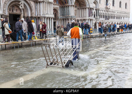 Venise, Vénétie, Italie. Nov 7, 2017. Acqua Alta marée haute de 115cm à partir de la lagune provoquant des inondations temporaires sur la Piazza San Marco. Passerelle, ou des passerelles, sont installés à la circulation des piétons. Deux ouvriers locaux au premier plan tirant leurs chariots à travers l'eau. Credit : Mary Clarke/Alamy Live News Banque D'Images