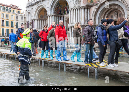 Venise, Vénétie, Italie. Nov 7, 2017. Acqua Alta marée haute de 115cm à partir de la lagune provoquant des inondations temporaires sur la Piazza San Marco. Passerelle, ou des passerelles, sont installés à la circulation des piétons. La femme porte sur la passerelle alors qu'elle s'arrête pour prendre un droit selfies sous l'œil attentif d'un agent de police locale. Credit : Mary Clarke/Alamy Live News Banque D'Images