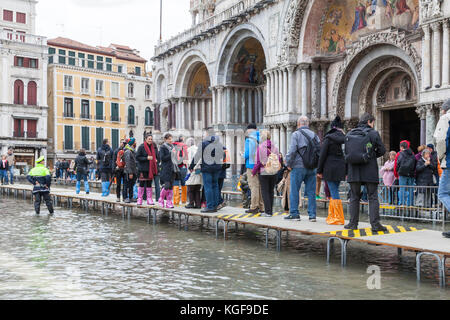 Venise, Vénétie, Italie. Nov 7, 2017. Acqua Alta marée haute de 115cm à partir de la lagune provoquant des inondations temporaires sur la Piazza San Marco. Passerelle, ou des passerelles, sont installés à la circulation des piétons avec des gens marcher en face de la Basilique de San Marco vu par le bureau de la police locale. Plusieurs portent des couvre-chaussures jetables en plastique colorés . Credit : Mary Clarke/Alamy Live News Banque D'Images