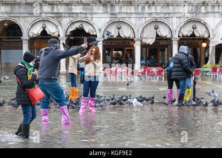 Venise, Vénétie, Italie. Nov 7, 2017. Acqua Alta marée haute de 115cm à partir de la lagune provoquant des inondations temporaires sur la Piazza San Marco. Les touristes en jouant avec les pigeons dans l'eau avec des oiseaux posés sur la tête et les bras. Credit : Mary Clarke/Alamy Live News Banque D'Images