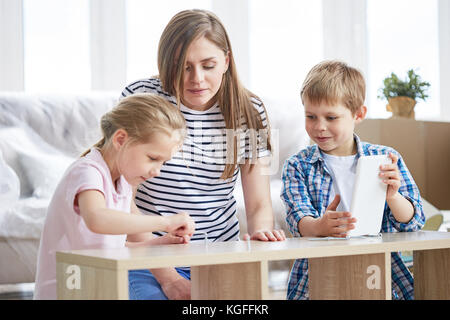 Séduisant jeune mère et ses enfants mignon bénéficiant d'entreprise alors que les autres se sont réunis dans la salle de séjour et montage de meubles Banque D'Images