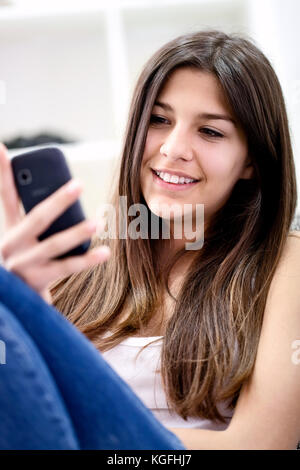 Smiling teenage girl consulte ses messages texte sur son téléphone mobile. Banque D'Images