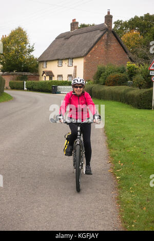 65 ans femme cycliste sur une route rurale, dans le village de Shapwick, Dorset. Banque D'Images