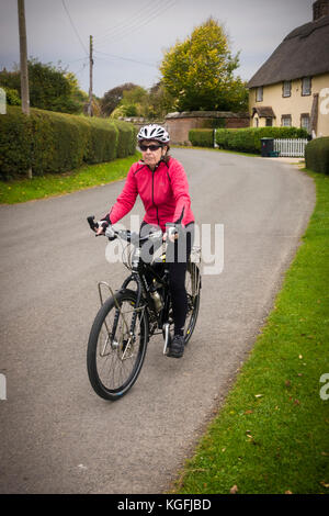 65 ans femme cycliste sur une route rurale, dans le village de Shapwick, Dorset. Banque D'Images