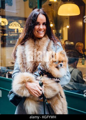 Portrait d'une femme souriante en manteau de fourrure, tenant un chien poméranien Banque D'Images