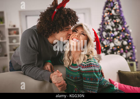 Couple aimant à chaud sur un confortable chandails de Noël Nouvel an, souriant, s'embrasser, de s'amuser avec les autres. Banque D'Images