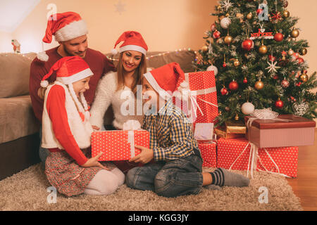 Beautiful happy family wearing santa hat et l'échange de cadeaux de Noël à la maison. Banque D'Images