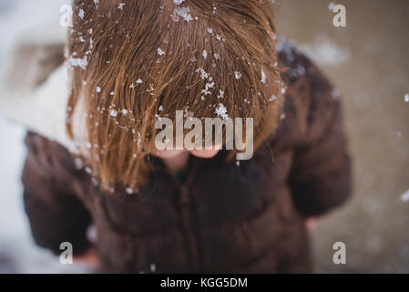 Regardant vers le bas sur un enfant en portant un manteau d'hiver avec de la neige dans ses cheveux au cours de l'hiver Banque D'Images