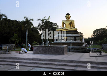 Parc Viharamahadevi Hunupitiva Colombo Sri Lanka homme priant devant grand Bouddha doré dans le Dhyana Mudra assis dans l'Ardha Padmasana positio Banque D'Images