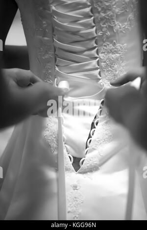 Bride standing avec son dos vers la caméra, les mains attacher sa robe de mariage, photo en noir et blanc Banque D'Images