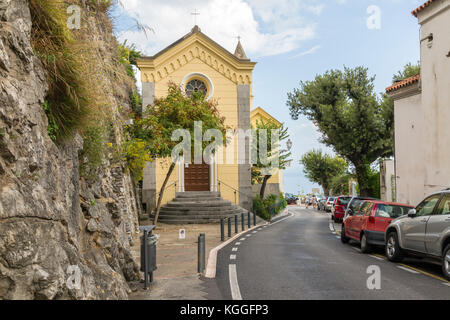 Amalfi Coast Road en passant par Positano avec une église d'un côté et les voitures en stationnement sur l'autre. Banque D'Images