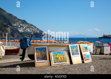 Art en vente affiché contre un bateau sur la plage de Positano, Italie Banque D'Images