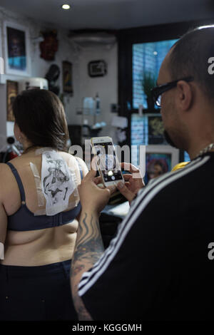 Un tatoueur au travail,un artiste de tatouage encres un conçu sur le dos d'une fille locale dans son studio à Londres. Banque D'Images