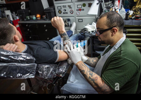 Un tatoueur au travail,un artiste de tatouage encres un conçu sur le dos d'une fille locale dans son studio à Londres. Banque D'Images