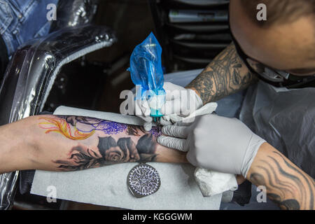 Un tatoueur au travail,un artiste de tatouage encres un conçu sur le dos d'une fille locale dans son studio à Londres. Banque D'Images