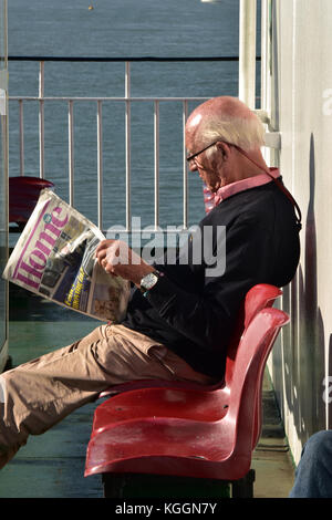 Un homme âgé d'âge moyen ou lire un journal tout en s'asseyant sur un siège sur le pont supérieur d'un ferry pour l'île de Wight. rattrapage. Banque D'Images