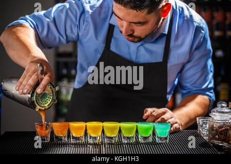 Douzaine de cocktails arc-en-ciel colorés en préparation sur le comptoir par un barman Banque D'Images