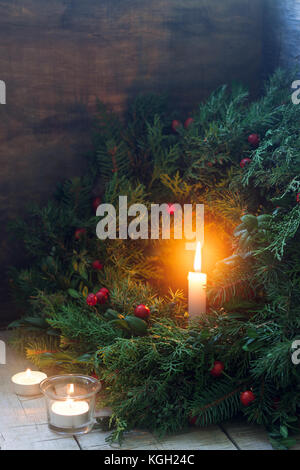 Une couronne de Noël faite de branches de sapin, genévrier, tuja, buis et Wild Rose baies. wreath with burning candles on a wooden background f sélective. Banque D'Images