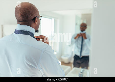 Man putting sur une cravate à la recherche à un miroir. Vue arrière d'un homme portant un collier. Banque D'Images