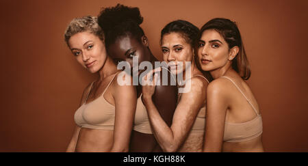 Groupe de belles jeunes femmes debout ensemble sur fond brun. Multi Ethnic woman looking at camera en studio. Banque D'Images