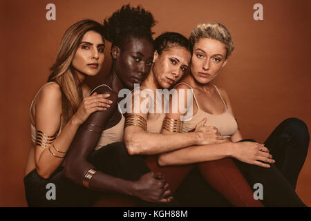 Groupe de diverses femmes siégeant ensemble contre le fond brun. Les femmes ethniques multiples avec différents tons de peau en studio. Banque D'Images