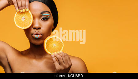 Jeune femme africaine avec des oranges et de maquillage artistique dans la main. Closeup portrait of female model sur fond jaune avec copie espace. Banque D'Images