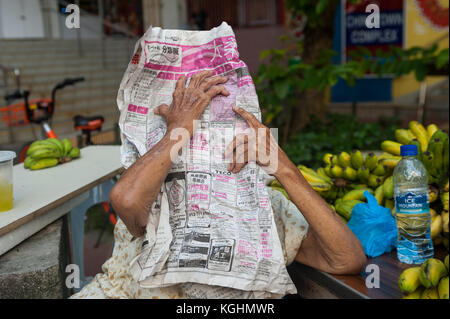 03.11.2017, Singapour, République de Singapour, en Asie - une vieille femme qui vend des bananes dans le quartier de Chinatown à Singapour se cache derrière un journal. Banque D'Images